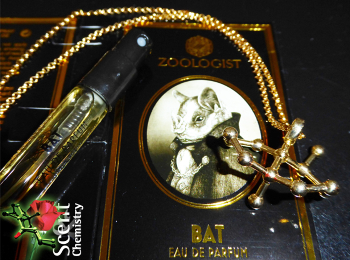 Geosmin 3d printed Geosmin pendant in polished brass on an 18k gold-plated Thomas Sabo KE1219-413-12-L42v necklace in front of a sample of 'Bat' (Zoologist Perfumes, 2015).